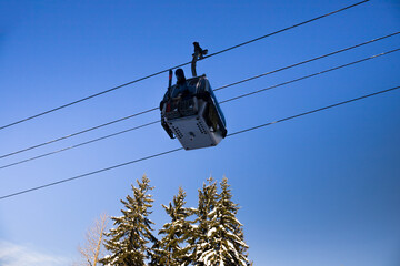 ski lift gondolas against blue sky over slope at ski resort on sunny winter day, snowy spruce forest