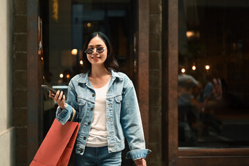 Asian woman holding shopping paper bags in hands walking outdoor at the shopping district of a city