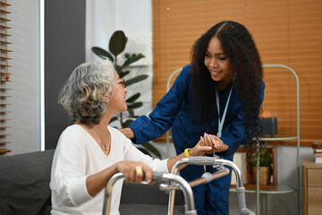 Fototapeta premium Attentive caregiver assisting, teaching senior woman to walk with walker. Assistance, rehabilitation and health