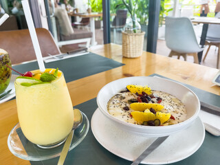 Mango smoothie and yoghurt granola bowl with fruits on cafe table. Healthy boost breakfast concept