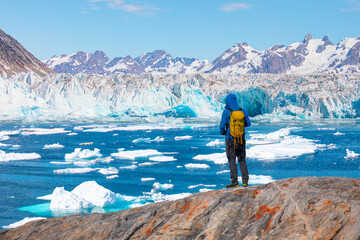 Environmental Concept - A Man Hiker looking at melting glacier - Melting of a iceberg and pouring water into the sea - Greenland - Tiniteqilaaq, Sermilik Fjord, East Greenland