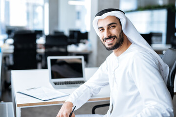 handsome man with dish dasha working in his business office of Dubai. Portraits of a successful businessman in traditional emirates white dress. 
