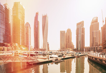 Fototapeta na wymiar View of high-rise buildings of residential district in Dubai Marina and yachts moored near pier in sunny day. Dubai Marina Towers. Flare sun, film effect, lens flare, glow, film light, flare