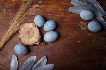 Blue painted easter eggs on brown wooden table with decorative silver feathers. Top view, copy space