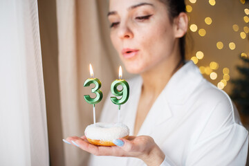woman holding a cake with the number 39 candles on festive blurred bokeh background