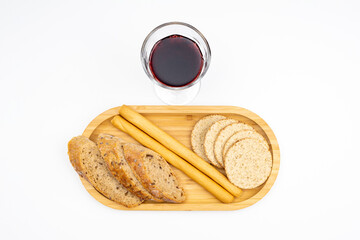 A glass of red wine and different types of traditional bread on a wooden tray on a white background