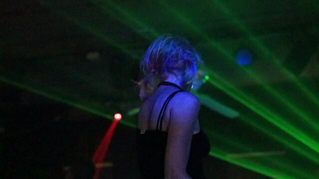 dancer sipping and grooving to the music in a dimly lit nightclub with blue-green pulsing laser lights. amusement, relaxation. A mature lifestyle is portrayed with a low angle slow motion.
