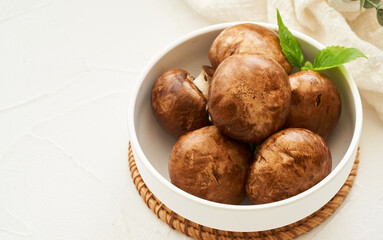 brown champignon button mushroom and green leaf in white bowl on white table background. pile of brown champignon button mushroom.                                                                   
