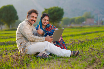 Indian farmer with wife using laptop at agriculture field.