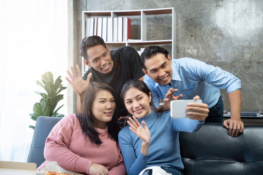 Friends watch sports on TV, cheer and celebrate. Happy diverse asian friend supporters fans sit on couch with popcorn and drinks. video call on mobile phone