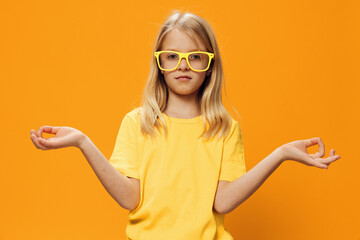 portrait of a cute beautiful school-age girl in yellow glasses for vision on a yellow background, pleasantly smiling looking at the camera and spreading her arms to the sides