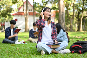 Charming Asian female enjoys listening to music through her headphones while sitting in the park.
