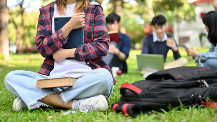 Female college student holding her tablet, sitting on grass in campus's park. cropped image