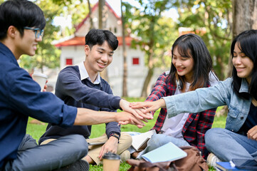 A group of happy Asian college students sitting in the park, putting their hands together, cheering up.
