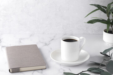 Cozy morning, with cup of coffee, book, eucalyptus twigs, flowerpot in decor on a white stone table. Scandinavian style, lagom. Balanced lifestyle concept. Horizontal, copy space.