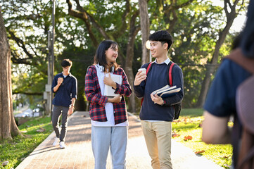 Happy Asian female college student talking with her male friend while walking in the campus's park