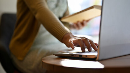 cropped image, A female using laptop, typing on keyboard, remote working in the coffee shop.