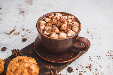 Hot chocolate drink with marshmallows in a cup and sweet bakery eclair dessert sprinkled with cocoa powder on white table