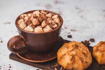 Hot chocolate drink with marshmallows in a cup and sweet bakery eclair dessert sprinkled with cocoa powder on white table