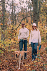 young happy cheerful couple playing with their labrador retriever dog outdoors in autumn forest. Family with a pet having fun