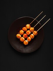 Spicy skewered chicken meatballs on the brown plate in black background