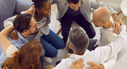 Diverse multiracial young people sit in circle, hugging and showing unity at group psychological or counselling session. Group psychotherapy, therapy, psychological help, mental health and support.