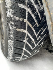 Close up pf the black winter tire of a car with some snow and ice in the winter tread 