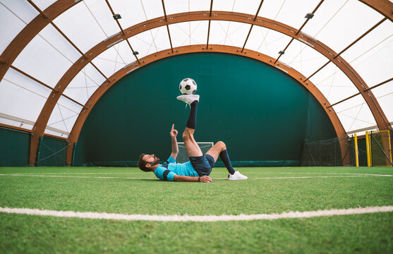 Cinematic image of a soccer freestyle player making tricks with the ball on a artificial grass court indoor. Concept about sport and people lifestyle	