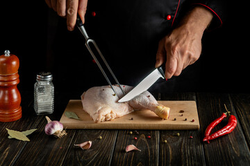 Cooking chicken legs in the kitchen. The chef cuts a raw chicken leg with a knife on a cutting board. Grilled chicken recipe concept