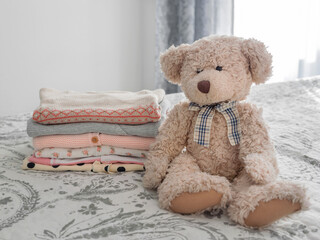 a stack of children's things and a teddy bear, knitwear, clothes made of cotton and natural materials on a gray-white background.