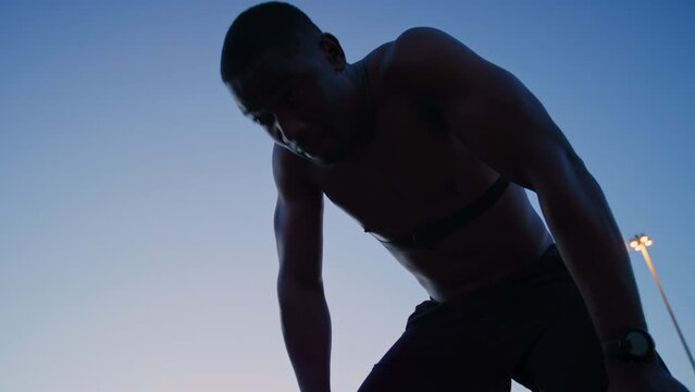 Running, night exercise and black man on break after .training in city. Low angle, workout and tired, fatigue or exhausted male athlete resting and spitting outdoors after jog, exercising or cardio.