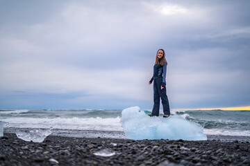 young woman standing and smiling on big piece of ice at diamond beach in iceland