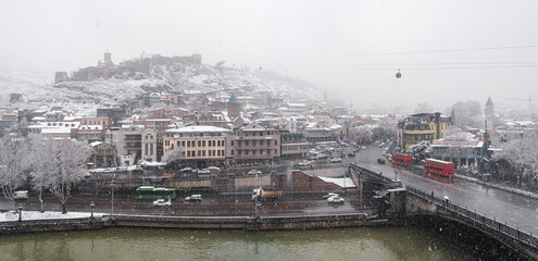 Snowy Tbilisi, Georgia. The central part of the Old City in the snow. Cable-car over Narikala Fortress and Metekhi bridge. 