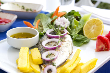 Roasted fish garnished with lemon slices served with vegetables