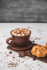 Hot chocolate drink with marshmallows in a cup and sweet bakery eclair dessert sprinkled with cocoa powder on white table