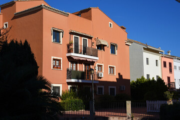 Facade of a residential building with windows and a balcony and apartments. Green trees in the garden near the wall of the house. Buildings minimalistic architecture. Home facade in Port Saplaya..
