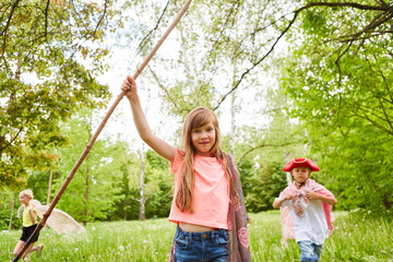 Girl holding stick and cape while playing with friends