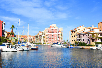 Jetty with yacht. Yachts and motor boats in marina Port Saplaya, Valencia. Yacht and fishing motorboat in yacht club. Colourful houses with apartments at coast Mediterranean Sea. Sailboat near pier.