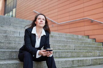 Confident businesswoman in her 40s sitting on stairs in city