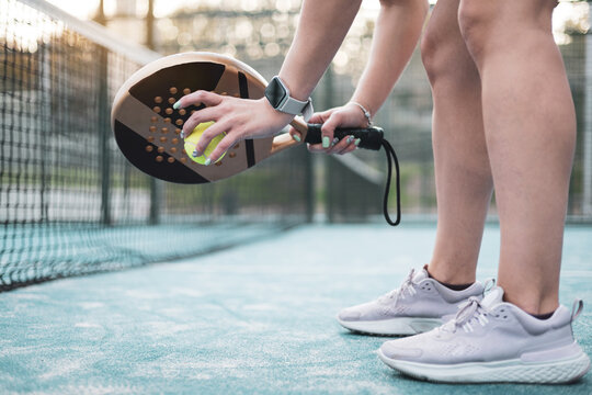 An unrecognizable girl picking up the ball from the ground on a paddle tennis court.