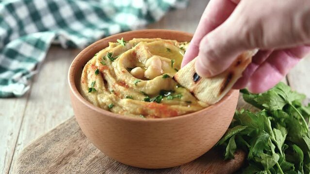 Man dipping chickpea hummus in bowl on wooden table