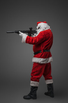 Shot of christmas santa claus with red costume and rifle against gray background.