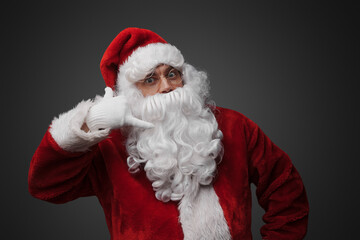 Studio shot of christmas santa with red suit and long beard pretending to talk on phone.