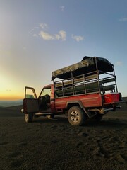 Pickup truck on dark black volcanic gravel during sunset. Pickup truck sunset scene. Sunset drinks. 'Cerro Negro' Nicaragua sunset scene. Volcano afternoon tour ending with drinks an the sun setting. 