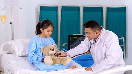 A male physician with a stethoscope is checking the heart rate of a teddy bear - a friendly doctor ...
