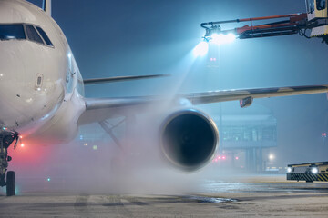 Deicing of airplane before flight. Winter night at airport during snowfall..