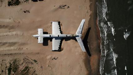 Military secret plane on the shore of the sea. Action. Aerial top view of an abandoned plane on a sand beach.