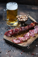 Cutting Spanish sausage fuet on a kitchen cutting board and glass of beer on dark wooden  background