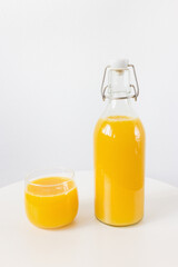 Fresh squeezed orange juice in bottle and glass on table on white