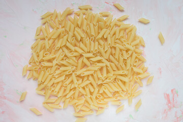 Raw Italian penne pasta on pink background